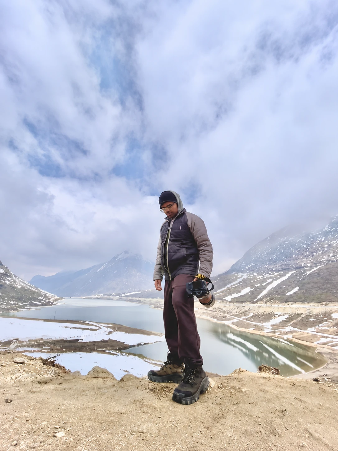 Sayantan Ghosh holding his camera beside a snowy mountain lake